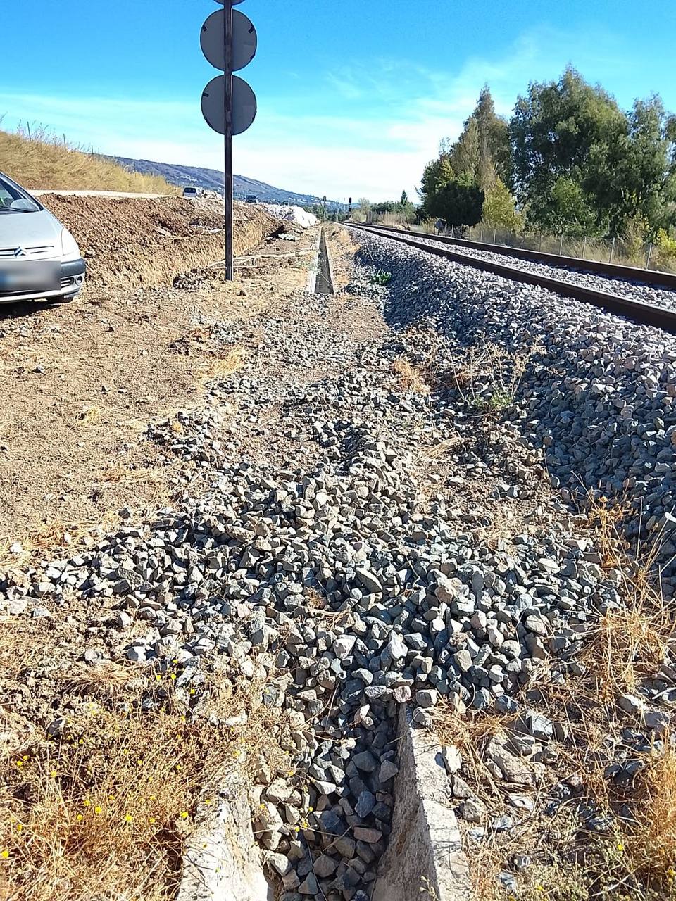 Cuneta de hormigón junto a la vía, colmatada de balasto y material de arrastre