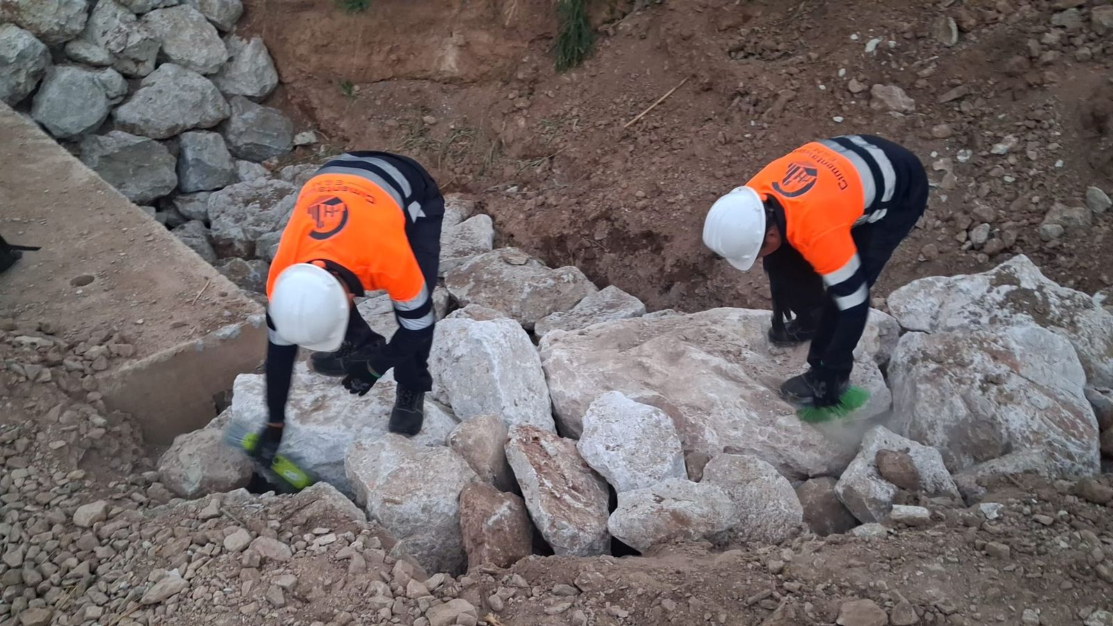 Dos operarios de Cimentaworks con casco y chaleco de la empresa trabajando sobre escollera junto a una obra de drenaje