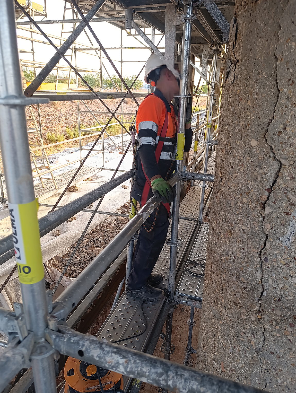 Fisura vertical en soporte de hormigón, inspeccionada desde plataforma de andamio con barandilla