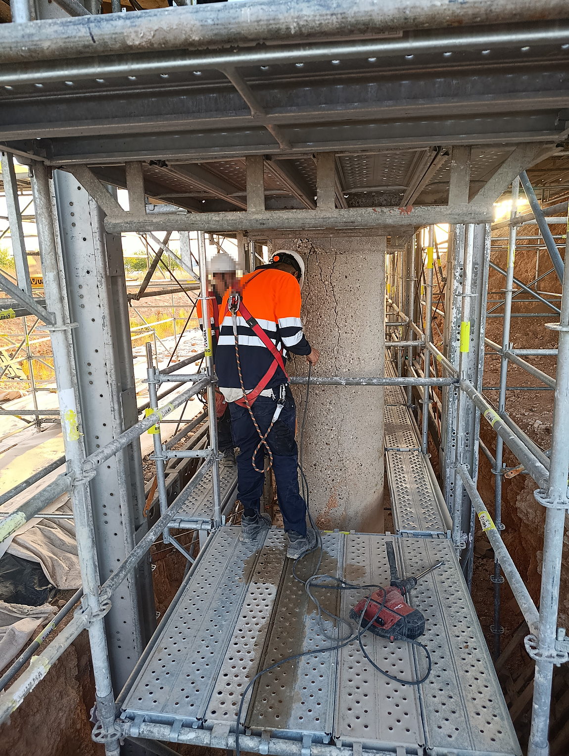 Operario taladrando el soporte de hormigón fisurado desde la plataforma de trabajo bajo el tablero